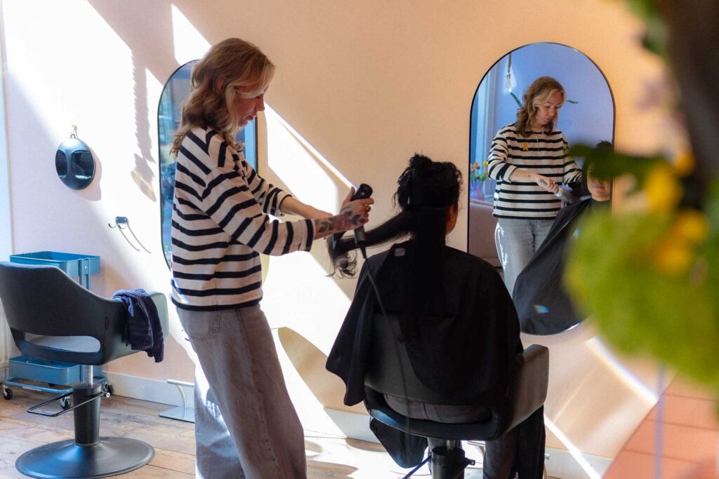 Kapster föhnt het haar van een klant in een stijlvolle salonsfeer bij Atelier HaarLAK in Nijmegen.